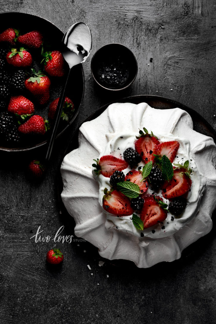 Meringue with strawberries and blackberries on top. Next to a bowl of berries. 