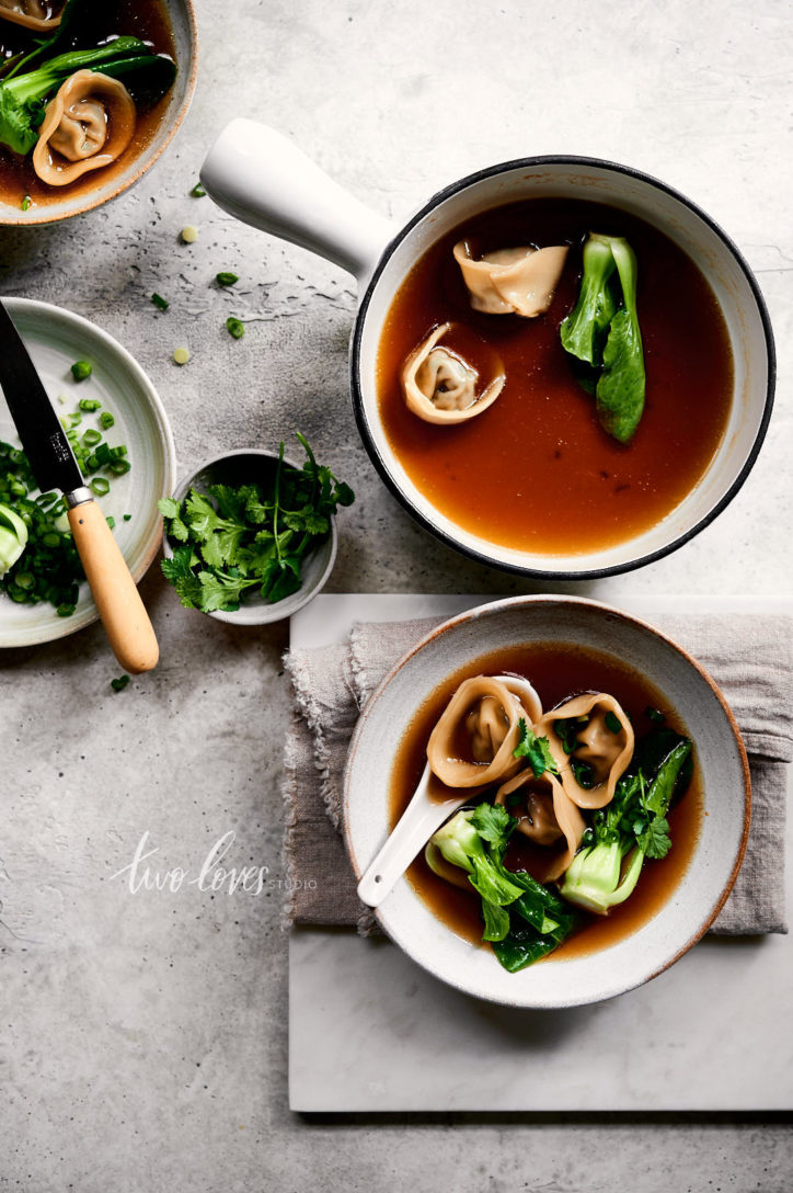 Overhead view of wonton soup with baby bok choy. Scattering of herbs and a napkin.