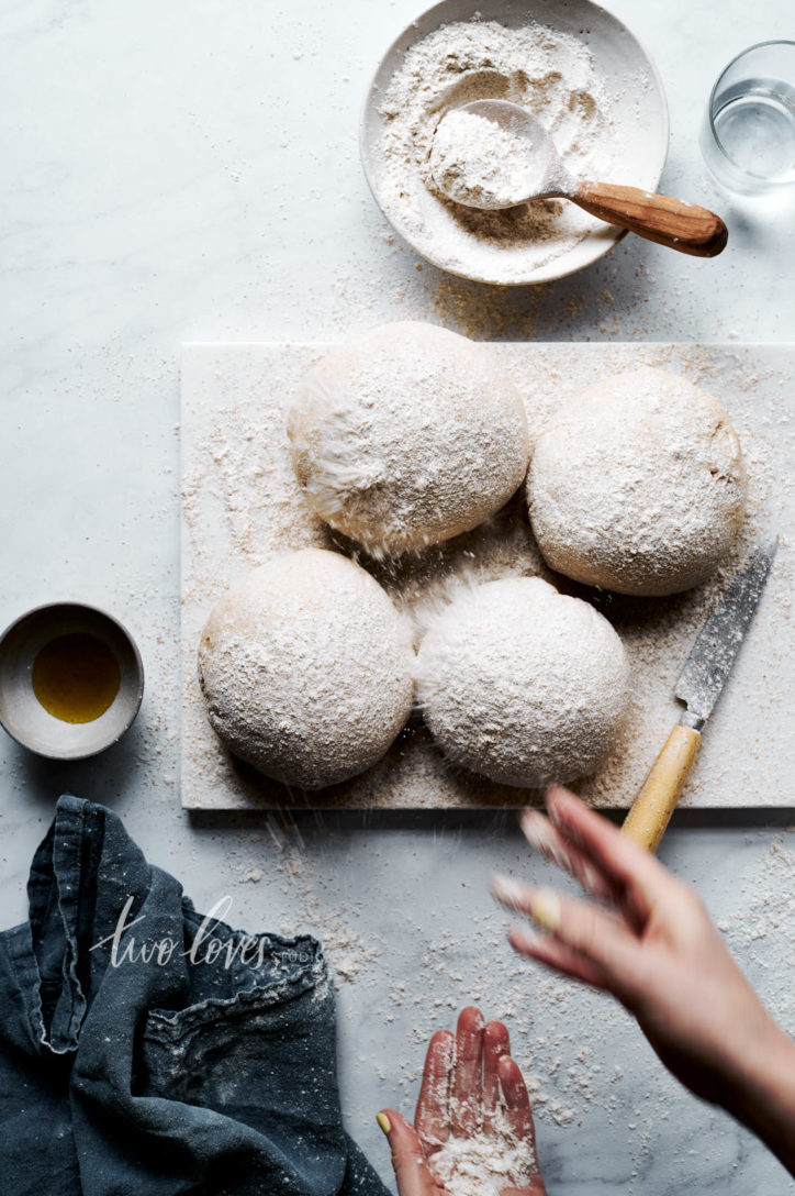 Four fresh rolled bread balls being dusted with flour. 