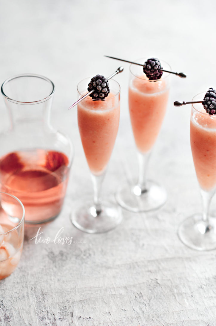 Three tall champagne glasses with frozen rose cocktail drink and blackberry garnishes. 