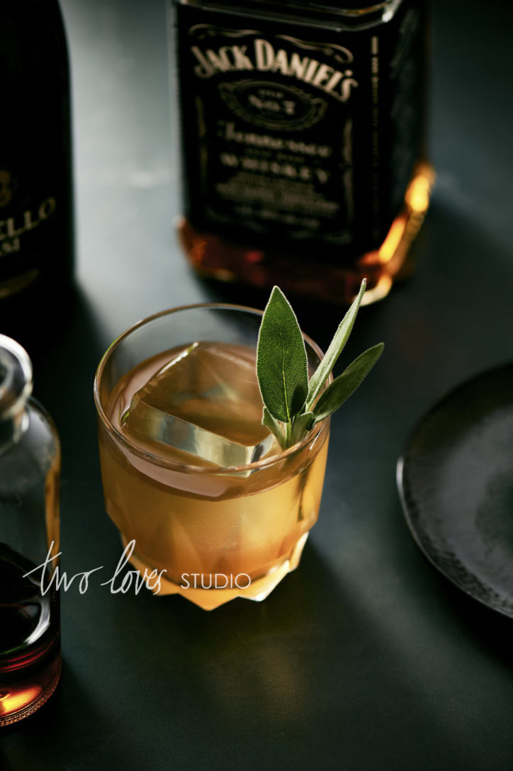 Whiskey in a small rocks glass with a single ice cube and mint leaves. 