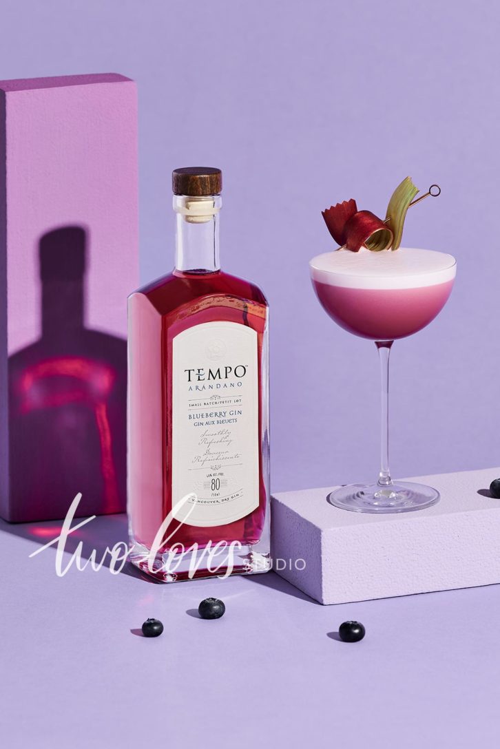 Tempo gin bottle next to a gin cocktail on a purple backdrop. 