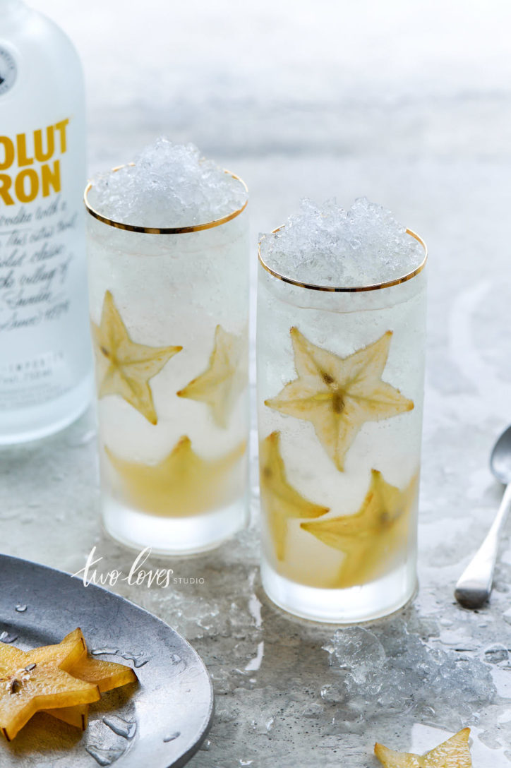 Two tall highball glass with crushed ice and star fruits placed around inside of the glass on a light backdrop.
