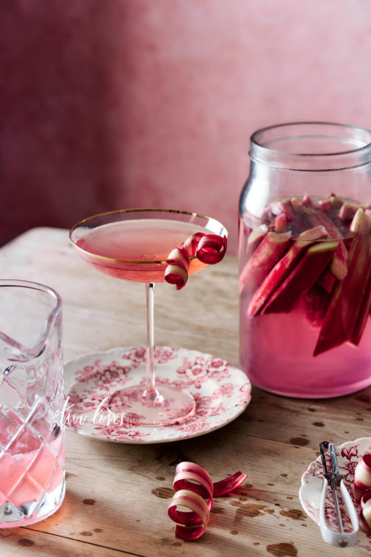 Pink Cocktail on a wooden table with a rhubarb cocktail garnish.