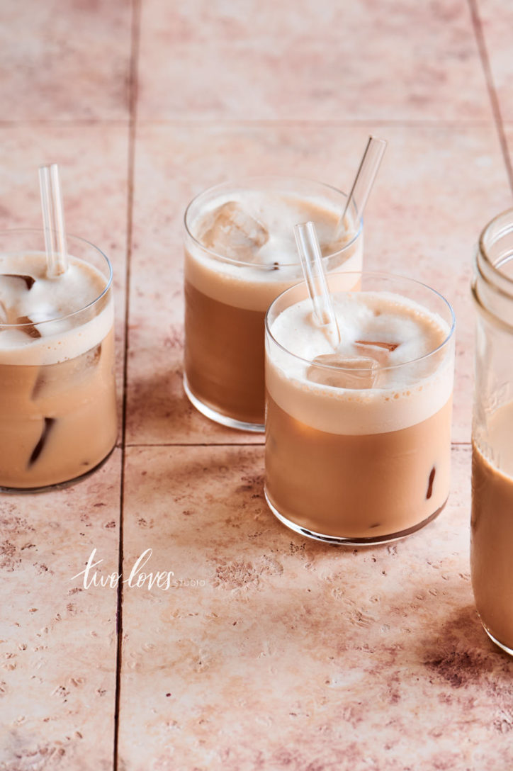 Brown tile background with three short no stem glasses filled with iced coffee.