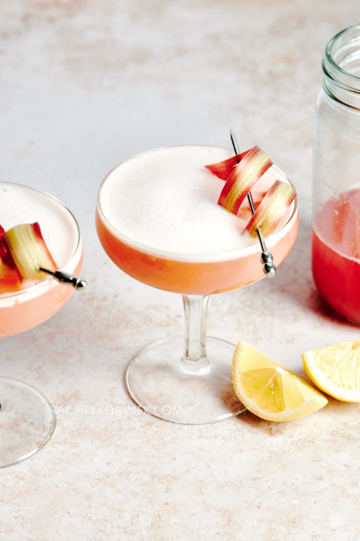 Two peach dry shake cocktails with a swirled garnish on the top and a wedge of lemon. 