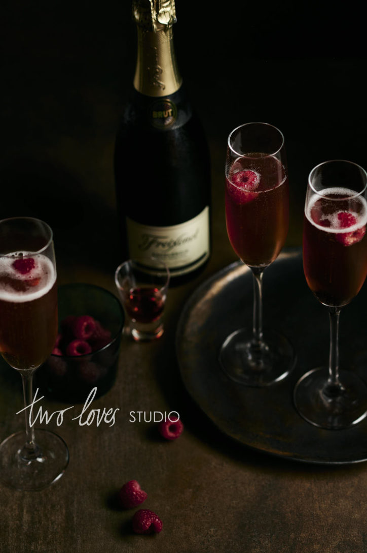 A wooden table with three champagne cocktails and raspberries garnishes. 