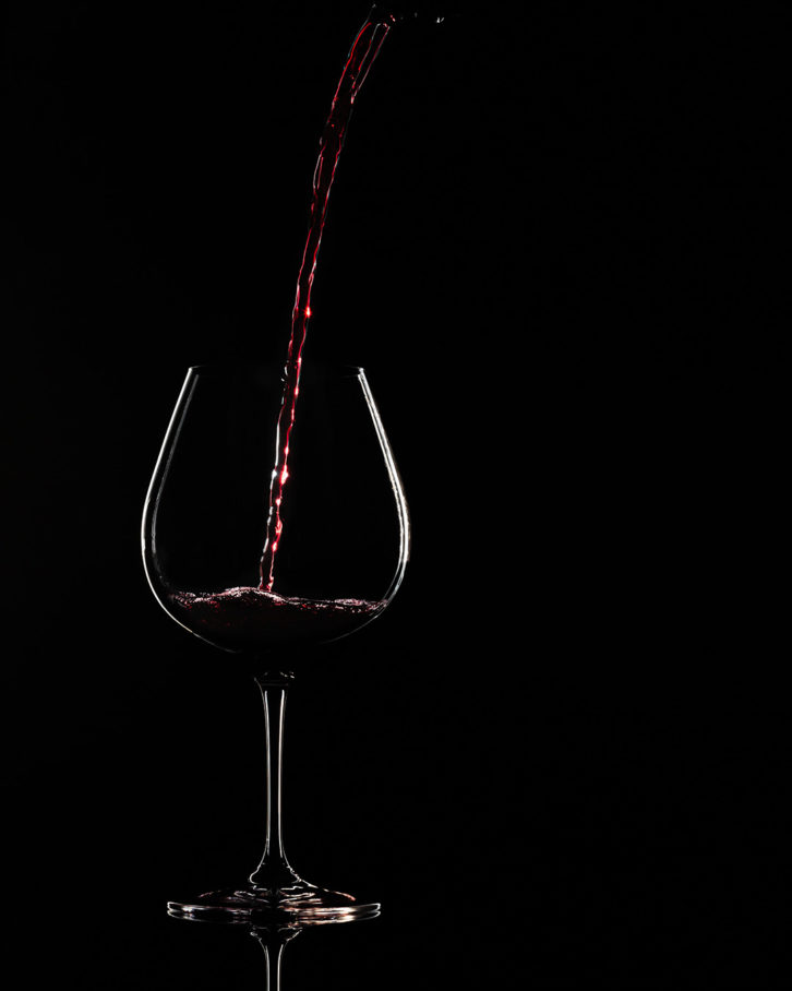 A black background with a large glass with red wine being poured in from the top right angle of the shot. This show was taken using the low key product photography set up.