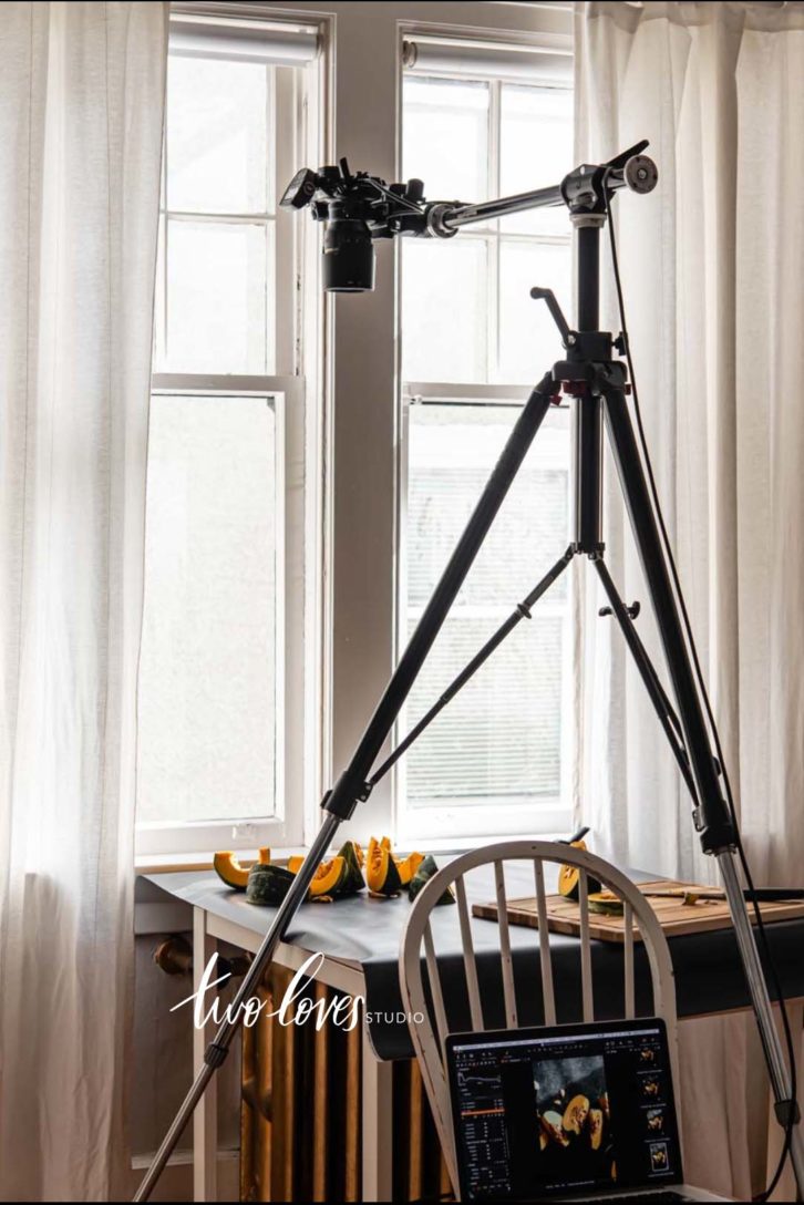 A tripod in full extension taking a shot of pumpkin cut into wedges with a cutting board and knife on a black background.