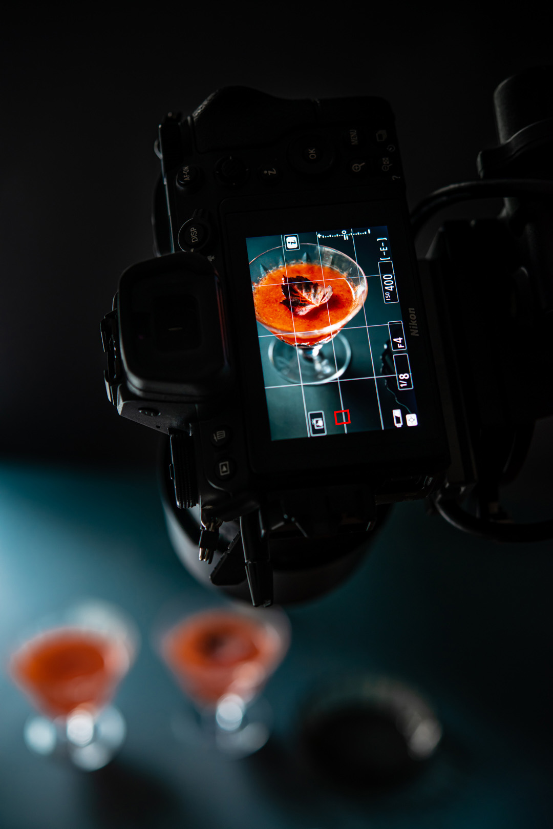 A red cocktail in a short martini glass through the view finder on the back of a camera.