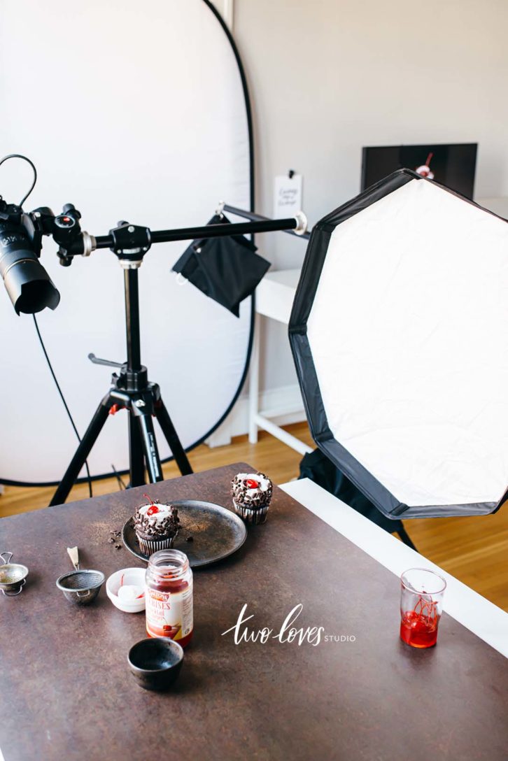 A shot of a one light photography setup, taking a photo of a chocolate cupcake on a dark brown background.
