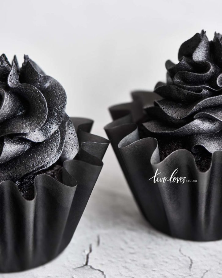 White cracked background with devils food cupcakes, black frosting and black cupcake paper holders. 
