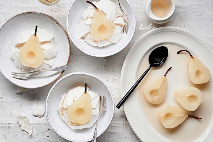 White textured background with white wine poached pears in white bowls and a side of poached pears on a white plate. 