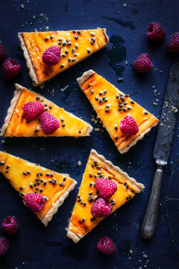 Image by Bea Lubas demonstrating her Food Photography Style. Dark blue background and slices of lemon meringue with garnishes of raspberries on top.  