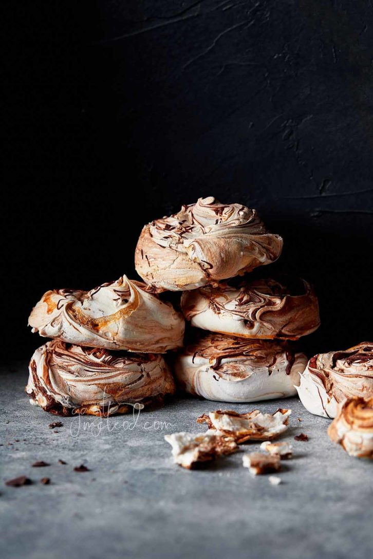 A black background with 6 meringues stacked in a pile on marble. Showing the range of depth and contrast by using photography flags. 