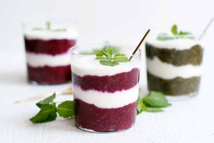 Three clear glasses on a white background with layers of yogurt and chai seeds. Mint garnish on top.