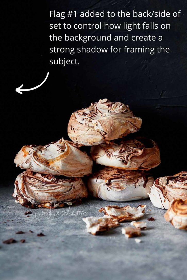 A black background with 6 meringues stacked in a pile on marble. Showing that no photography flags have been used demonstrating a lot of light falling on the scene resulting in a lack of depth. 