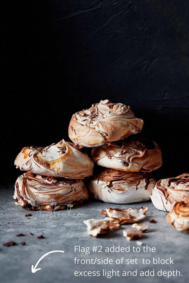 A black background with 6 meringues stacked in a pile on marble. Showing where to place a second flag to the front of the shot. 