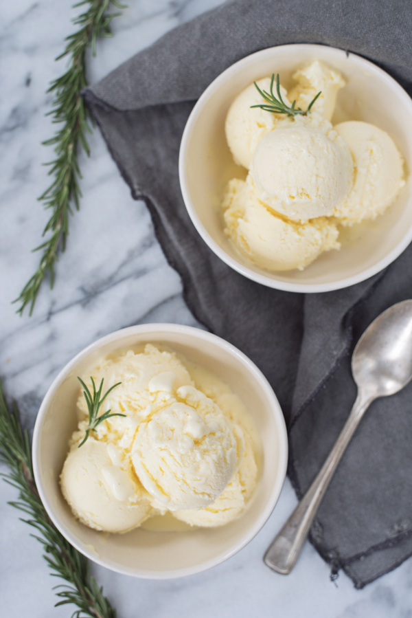 Marble background, two white photography prop bowls of ice-cream with a side of Rosemary as garnish. 