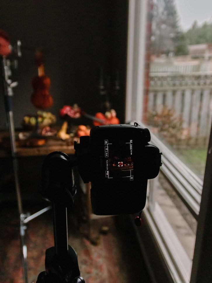 Example of chiaroscuro effect in food photography. A wooden table with fruit, black candle sticks and a violin and the camera setup.