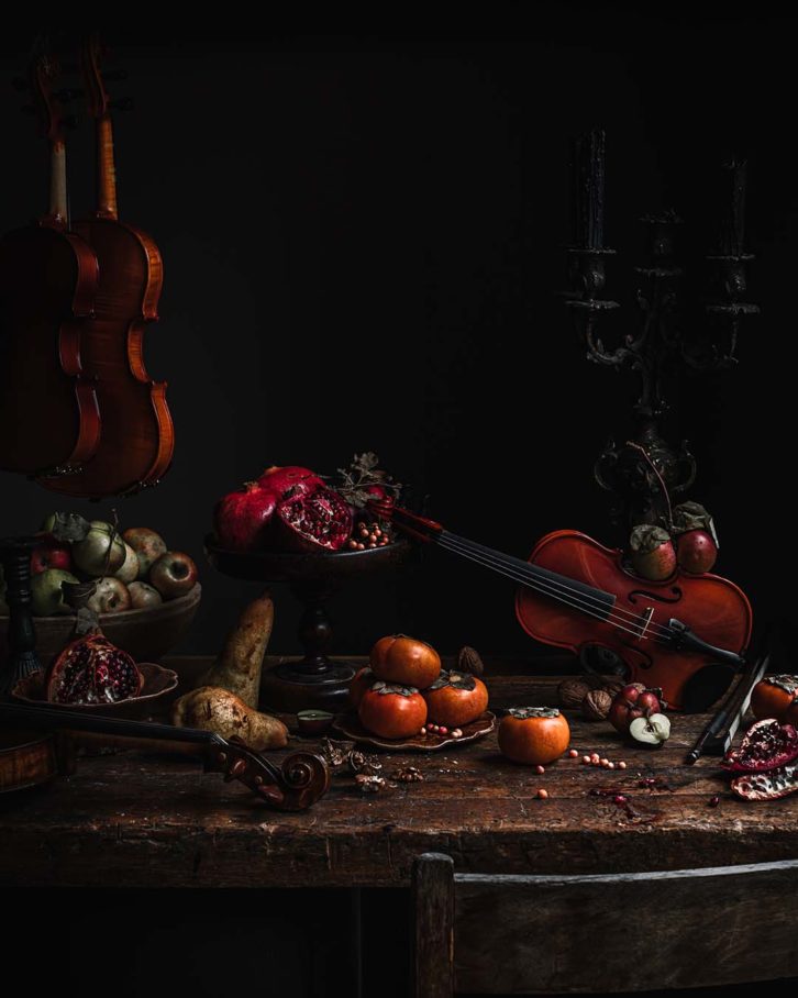 Example of chiaroscuro effect in food photography. A wooden table with fruit, black candle sticks and a violin. 