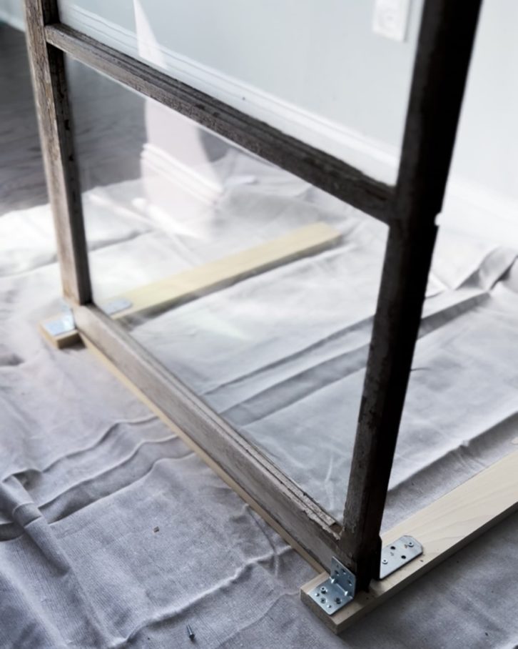 White table cloth on the ground, with two planks of wood, two bracket frames to hold the window in place. 