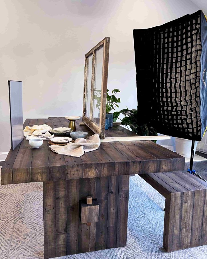 A dinning room table with the faux window, a light box behind it. An assortment of plates and items on the table.