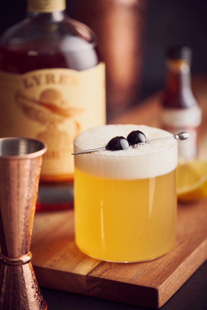 Virgin amaretto sour in a thin walled clear glass, on a wooden chopping board. 