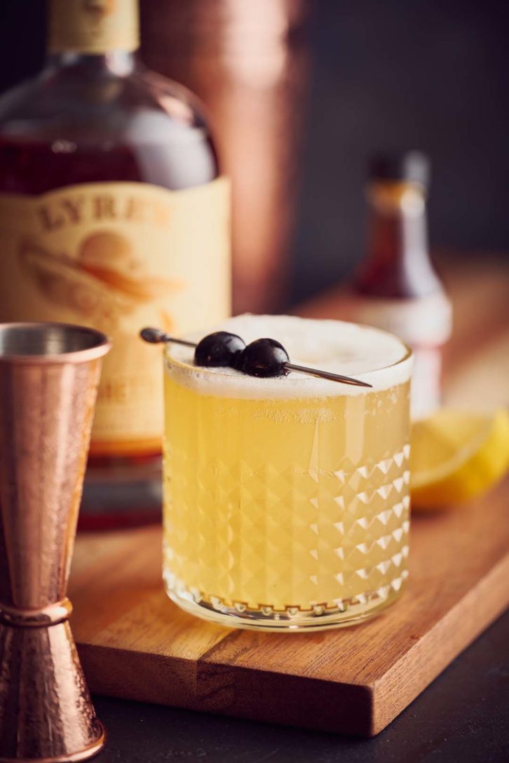 Virgin amaretto sour with a cherry garnish in a glass with texture, on a wooden chopping board showing how to avoid reflections in photography.