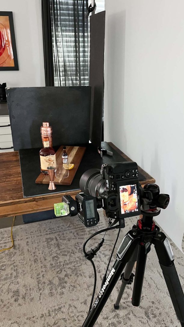 Close shot of a home set up showing a table with props, camera and lighting box and diffuser sheet. 