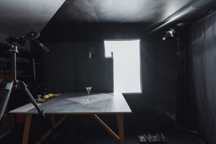 Camera set up at an angle, capturing a single martini glass on a dark grey background. 