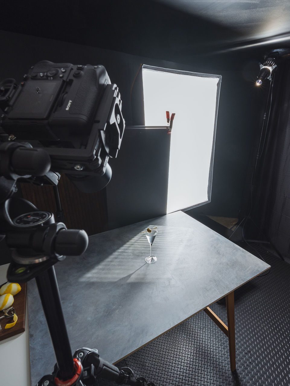 Camera taking a photo of a single moody martini glass on a dark grey background. 