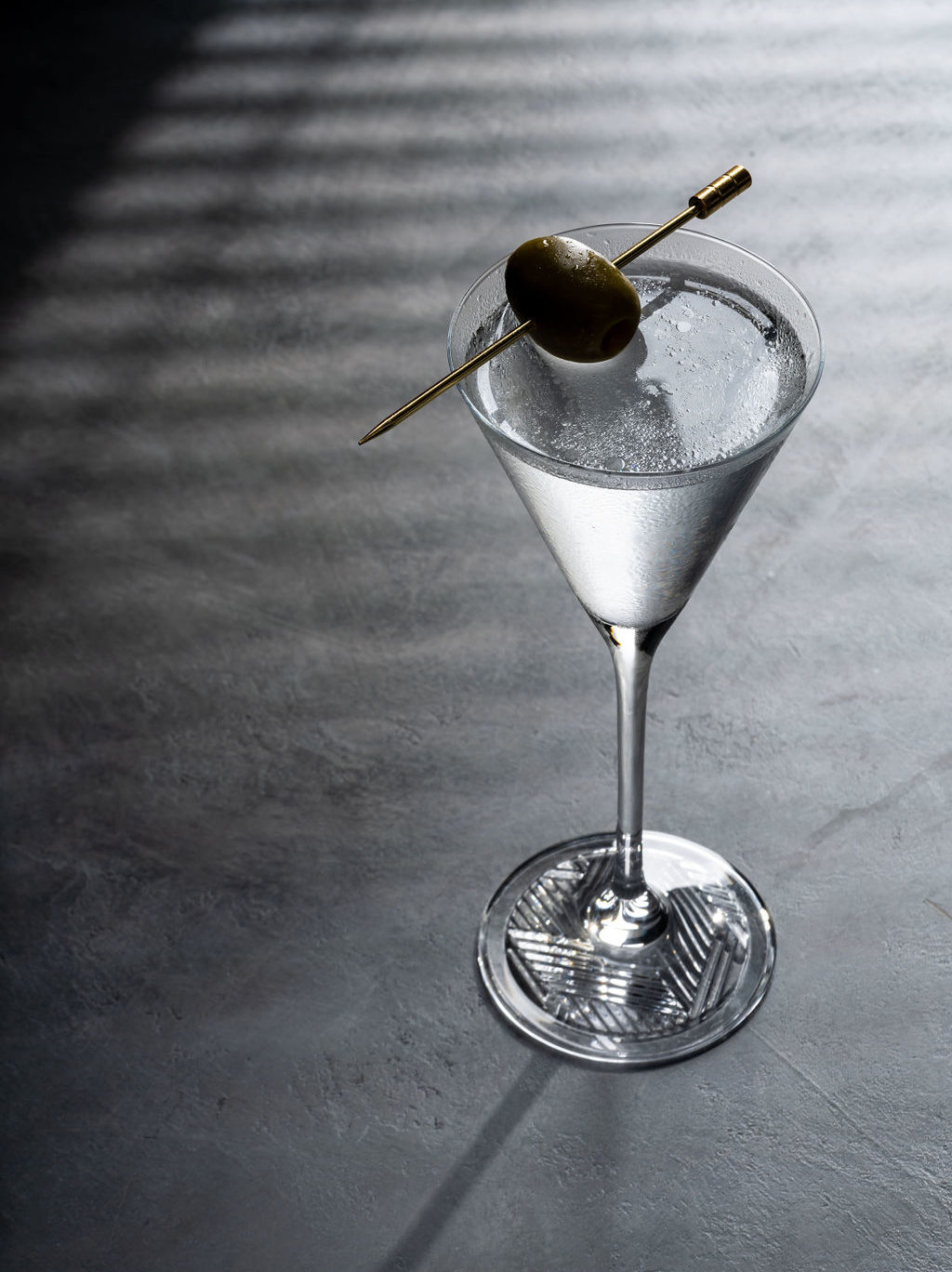 Dark background, with a moody martini and a single olive garnish. 