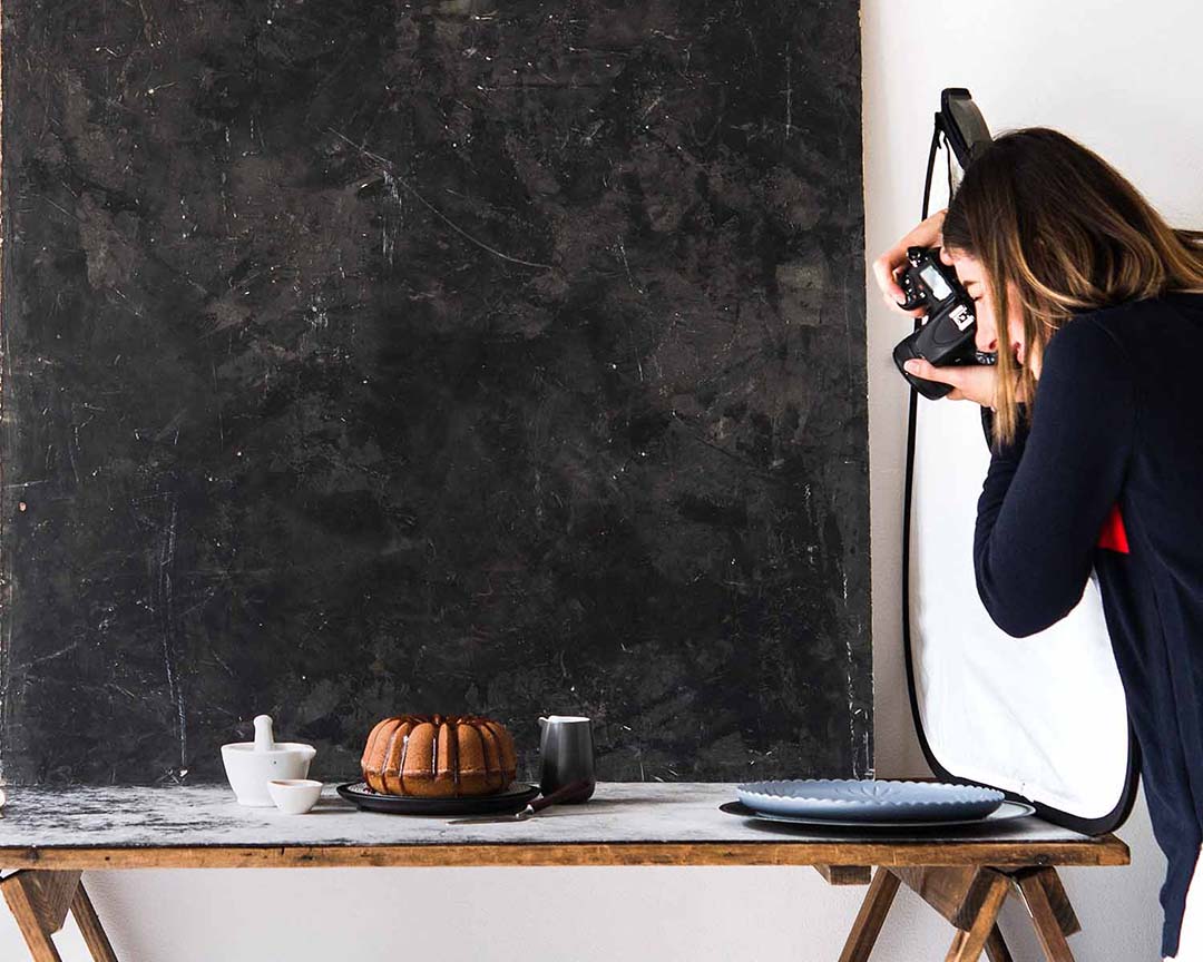 A person taking a photo of a bunt cake photoshoot on a wooden table showing sharp food photos.