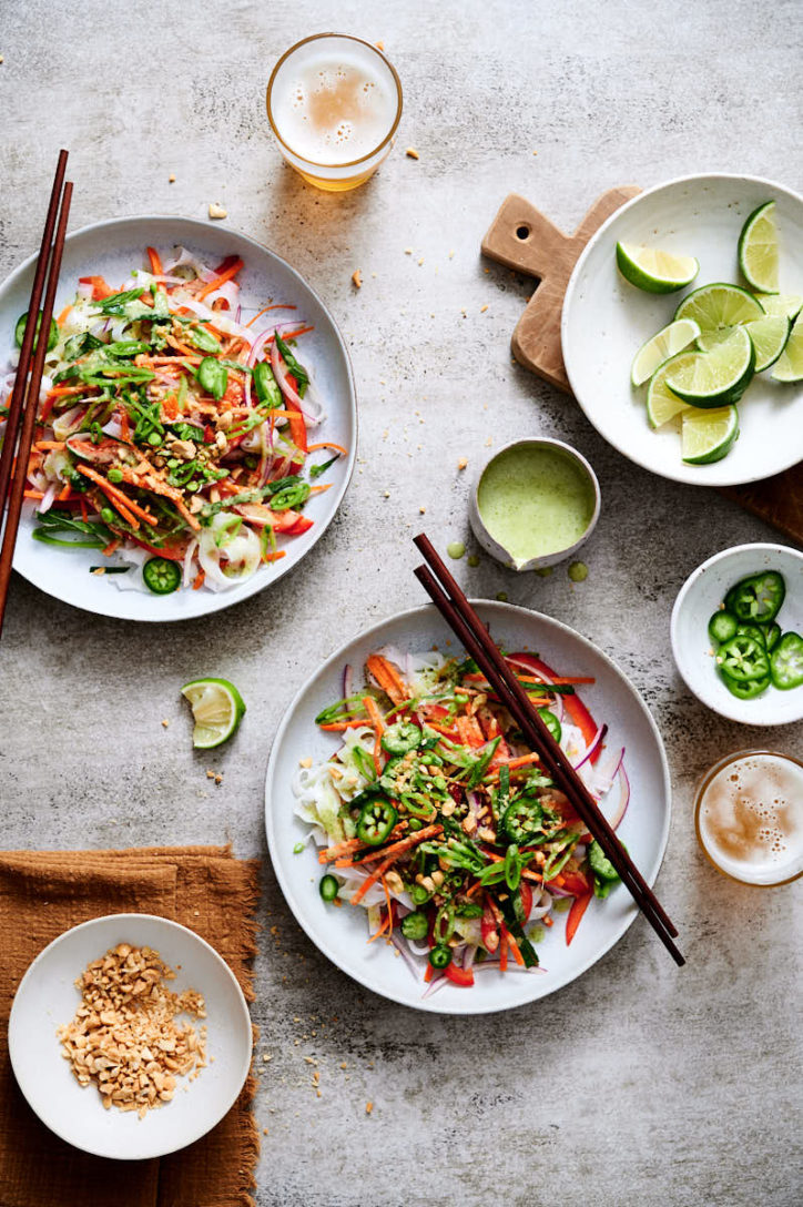 Two white plates with thai noodle salad and lime wedges. 