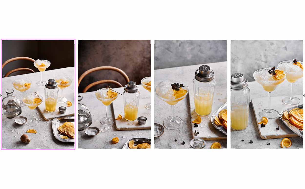 Orange cocktail in a martini glass with a glass cocktail shaker on a grey stone backdrop.  