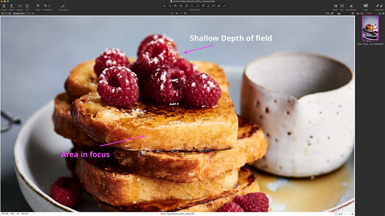 White bowl with french toast and raspberries and a small pot of syrup.