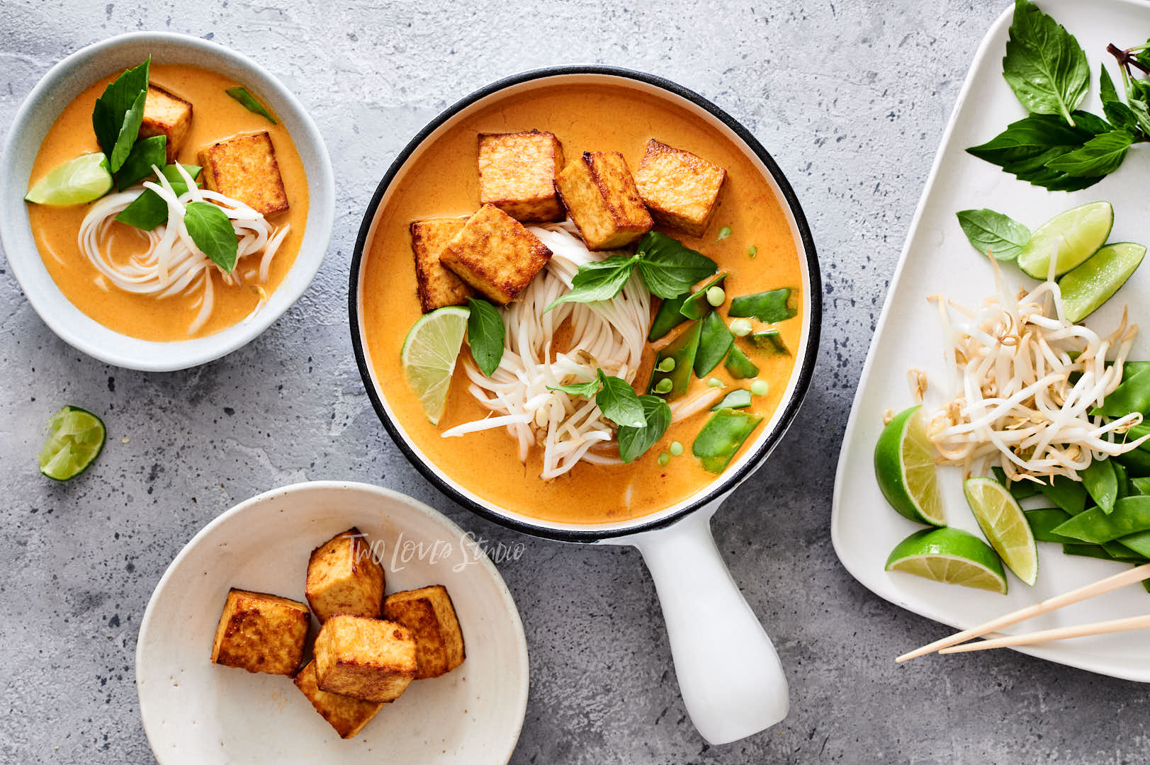 Assortment of ingredients, limes, beans, tofu and mint for styling noodle bowls. With a white noodle bowl.