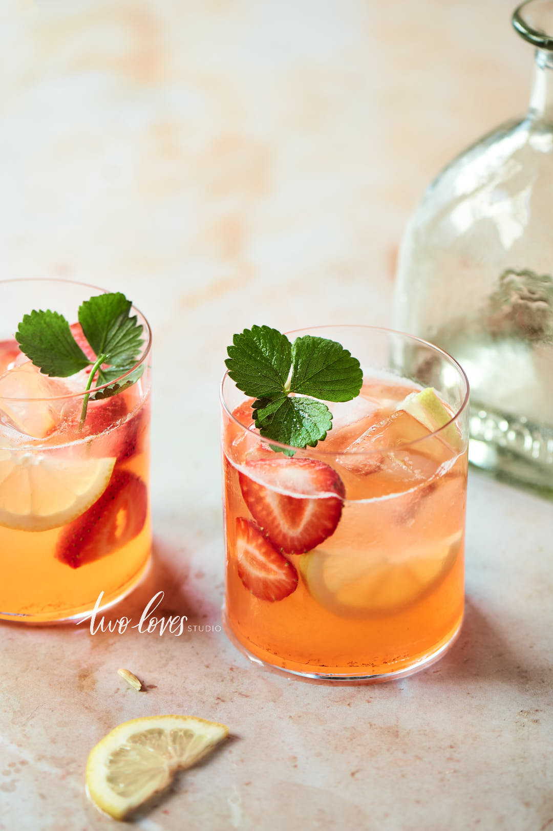 Marble background with a clear glass tequila bottle and two fruit cocktails in the foreground