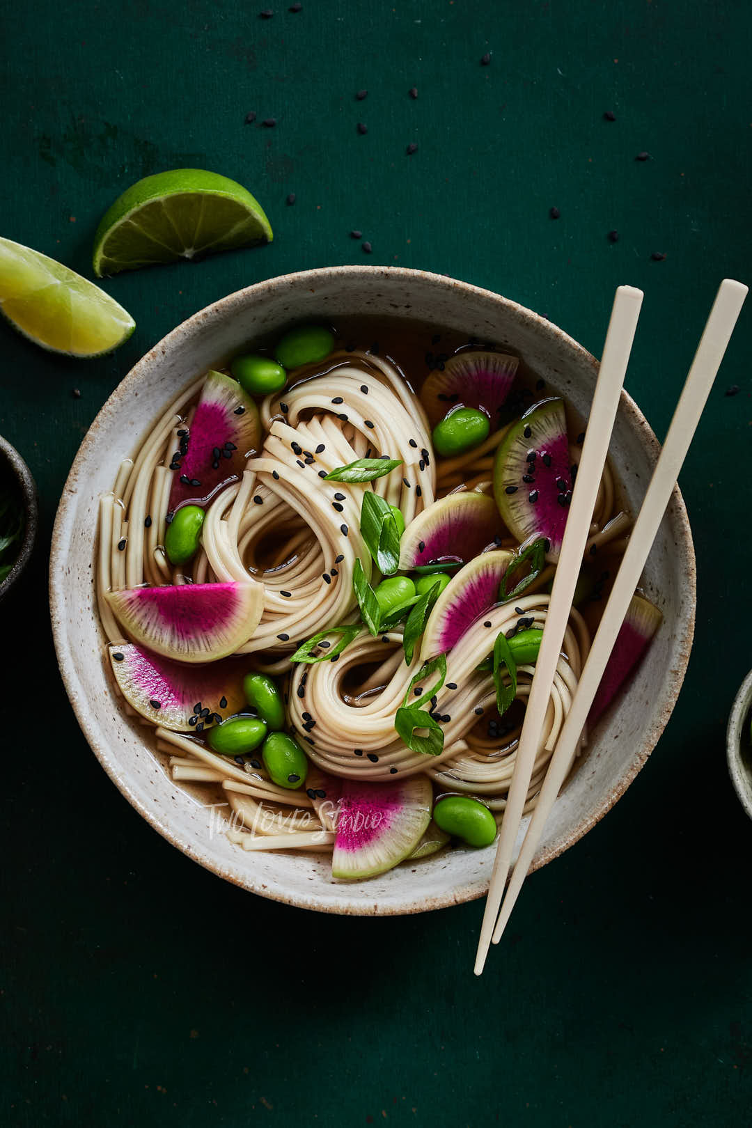 Dark green background with a large noodle soup bowl, ramen noodle nests with slices of radishes. 