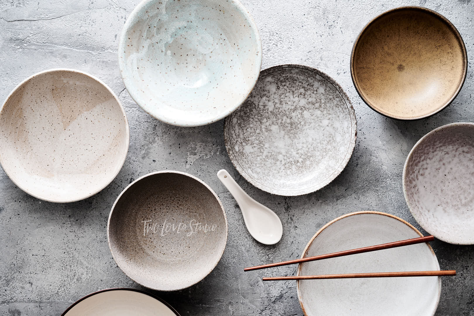 Concreate inspired background with an assortment of bowls and plates, chopsticks and spoons for styling noodle bowls. 