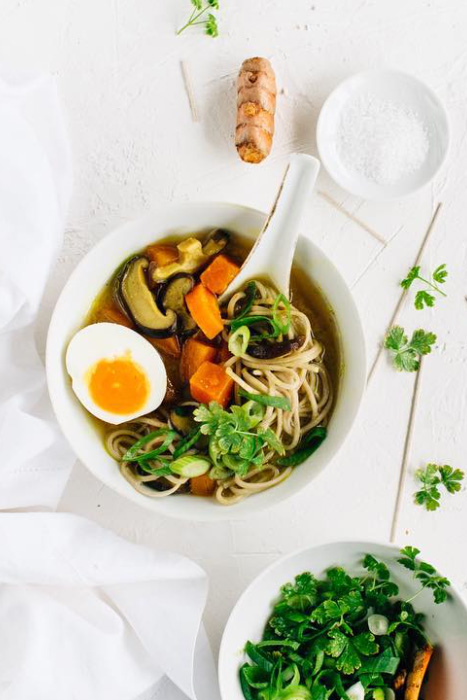 White background with a large white soup bowl with noodles, mushrooms and half an egg. Cilantro garnish. 