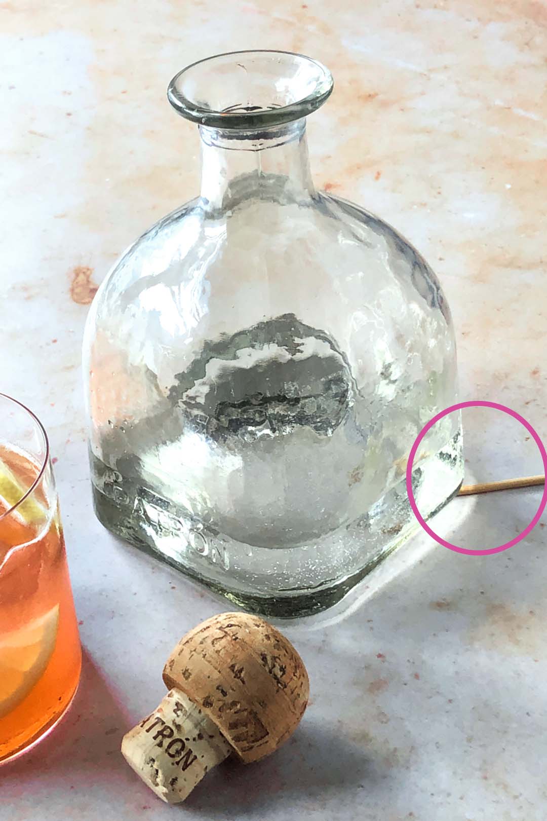 Marble background with a clear glass tequila bottle and a cork in the foreground
