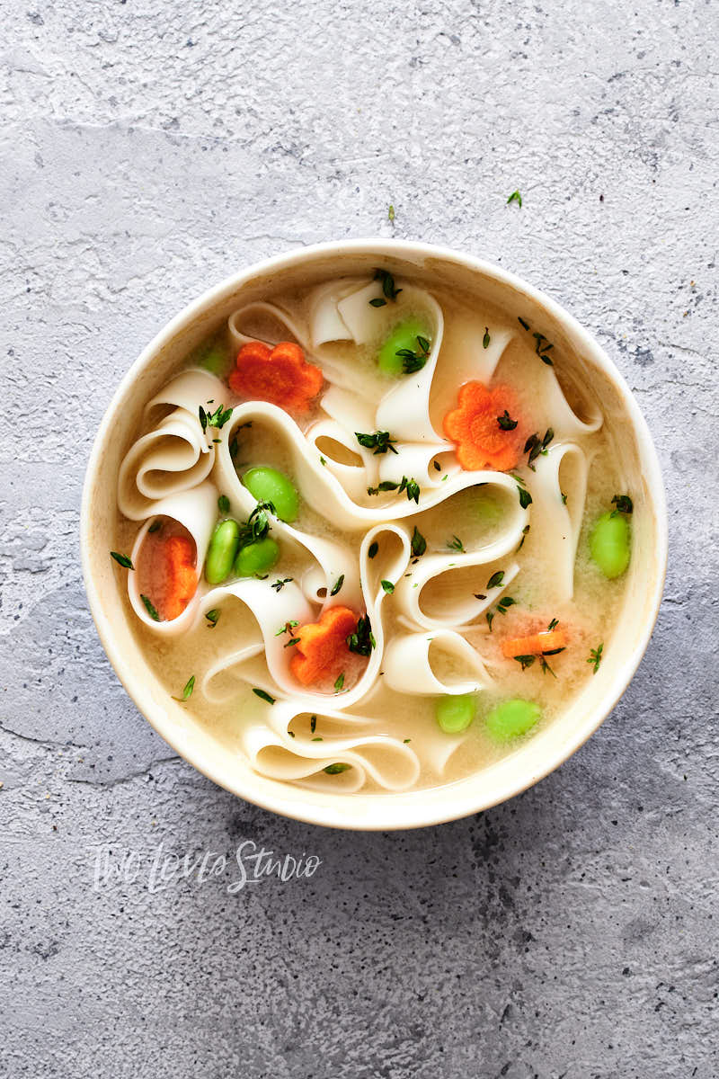 A noodle soup bowl with edamame and carrots.
