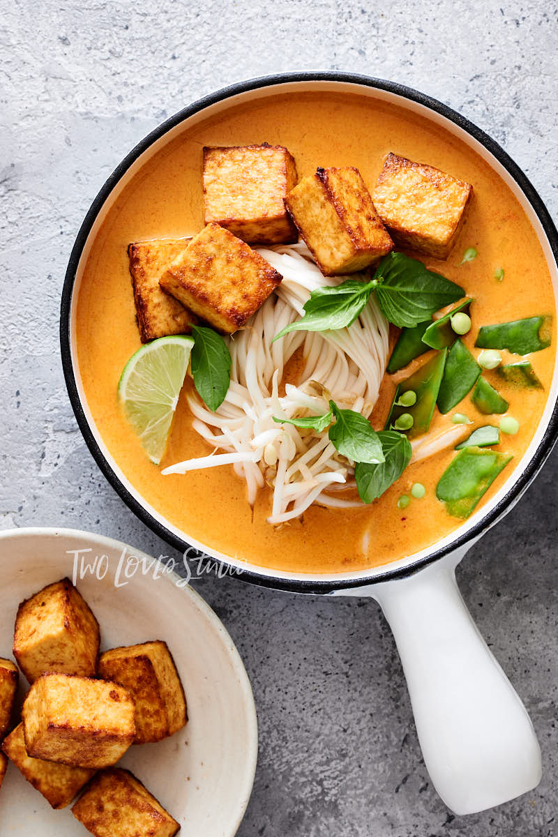 A laksa noodle soup bowl in a small pot with lots of toppings. An example of noodle food styling.