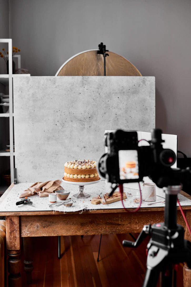 Behind the scenes photo of a wooden table with a sponge cake, cream filling. 