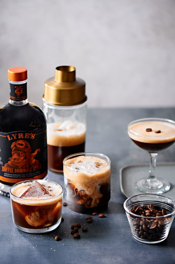 Three cocktail glasses with a non-alcoholoic iced coffee cocktail and a bottle of Lyres Coffee Originale Liquor.