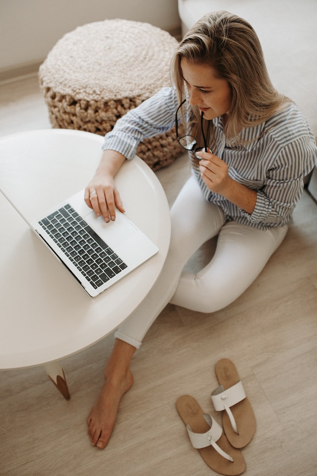 Girl sitting on the floor working on a laptop working on food photography pricing tips