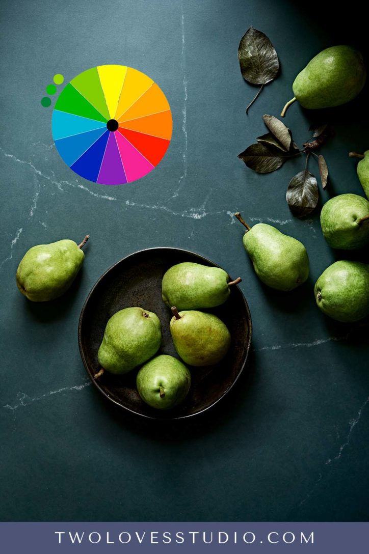 Dark green background with green pears in a black bowl. 