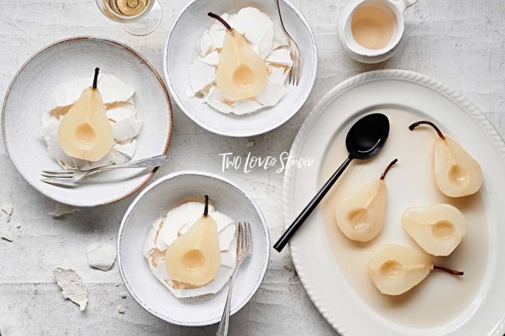 White background with pears in bowls ontop of meringues. 